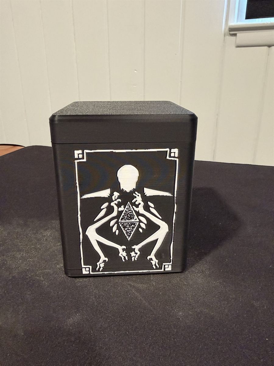 A black 3D-printed deck box with a raised white skeletal figure on the front