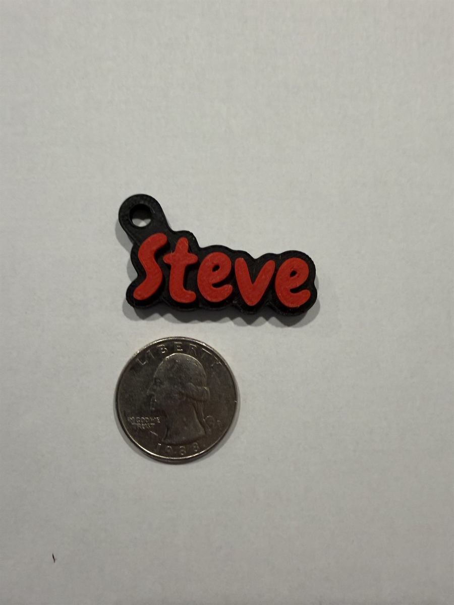 A red and black 'Steve' keychain next to a U.S. quarter for size reference