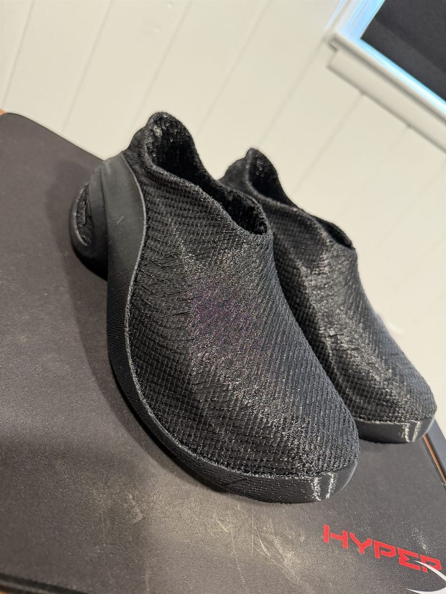 A pair of black 3D-printed slip-on shoes with a textured, knit-like flexible upper
